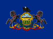 Pennsylvania state flag featuring the coat of arms with two black horses, a bald eagle, and the motto Virtue Liberty and Independence on a blue background.