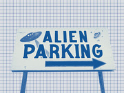 Blue-tinted photo of a novelty roadside sign reading Alien Parking with a UFO illustration and arrow, set against a grid paper background.
