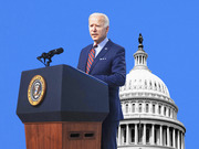 Editorial illustration of President Biden at a presidential podium with the US Capitol dome in the background on a blue backdrop.