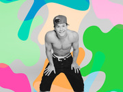Black and white photo of a shirtless young man in a backwards cap and jeans posed against a colorful abstract blob-shaped background.
