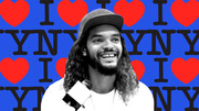 Black and white photo of a smiling man wearing a New York cap overlaid on a blue I Love NY pattern background with red hearts.