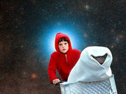 Editorial composite image of a boy in a red hoodie on a bicycle with a blanket-covered figure in the basket, set against a starry space background, referencing the film E.T.