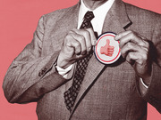 Black and white collage of a suited man pinning a button featuring a thumbs-up emoji onto his lapel, set against a pink background.