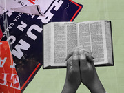 Editorial collage showing praying hands holding an open Bible alongside torn Trump campaign signs, illustrating religion and politics themes.