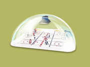 Editorial illustration of a miniature table hockey game enclosed under a transparent dome with a scoreboard floating above, set against an olive green background.