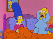 Animated still of Marge and Homer Simpson sitting in bed, with Homer appearing shocked or scared, from The Simpsons cartoon.