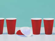 Illustrated scene of four red plastic party cups standing upright with one red cup and one white cup knocked over in the center, against a teal background.