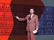 Colorized vintage photo of a TV news anchor pointing at an election results board showing candidate photos and vote tallies, tinted red and blue.