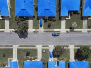 Aerial view of a suburban neighborhood with houses and cars digitally colorized in bright blue, used as editorial illustration.