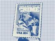 Blue-tinted editorial illustration of the McGruff the Crime Dog USA 20-cent postage stamp reading Take a Bite Out of Crime, set against a grid paper background.