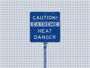 Blue-tinted photo of a road sign reading Caution Extreme Heat Danger on a grid paper background, used as editorial illustration.