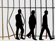 Editorial illustration showing three black silhouettes of people walking in front of rusty prison bars, suggesting themes of incarceration or criminal justice.