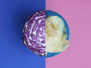 Split image showing half a red cabbage on a blue background beside a bowl of potato chips on a pink background, used as editorial art.