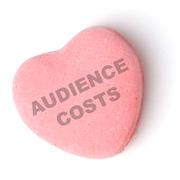 A pink candy heart with the phrase AUDIENCE COSTS stamped on it, styled like a Valentine's Day conversation heart candy.