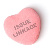 A pink candy heart with the phrase ISSUE LINKAGE stamped on it, styled like a Valentine's Day conversation heart candy.