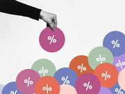 A hand picks up a pink circle with a percent sign from a pile of colorful circles all bearing percent symbols, illustrating the concept of interest rates or percentages.