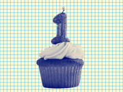 A blue-tinted cupcake with a number 1 candle on top, set against a grid paper background, used as editorial illustration.