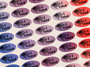 Decorative editorial illustration showing a repeating pattern of I Voted stickers transitioning from blue on the left to red on the right.