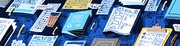 Editorial illustration showing scattered standardized test materials including ACT, SAT, and PSAT papers, exam books, pencils, and a calculator in blue tones.