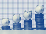 Four piggy banks of increasing size sitting on progressively taller stacks of coins against a blue grid background, illustrating savings growth.