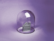 A small metallic house figurine enclosed under a glass bell jar dome against a purple background, symbolizing housing protection or isolation.