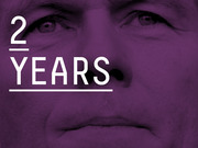 Purple-tinted close-up of a man's face overlaid with large white text reading '2 YEARS', used as an editorial graphic.
